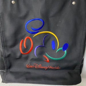 May include: Black tote bag featuring a colourful embroidered Mickey Mouse design and the text "Walt Disney World".