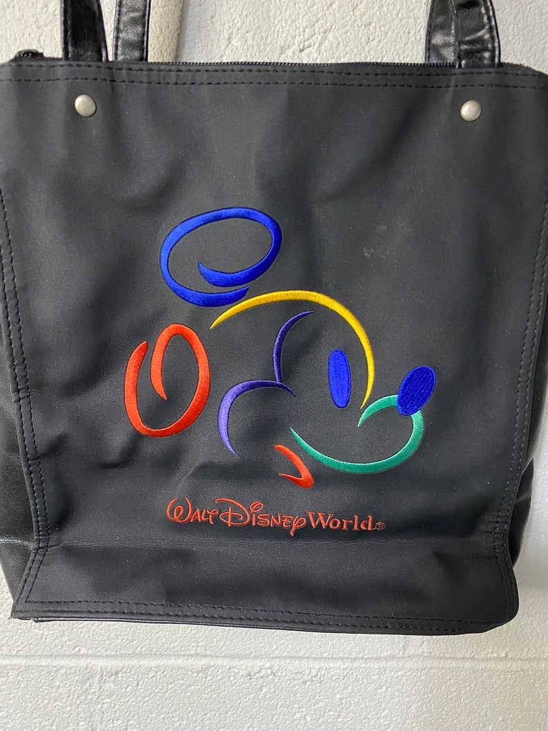 May include: Black tote bag featuring a colourful embroidered Mickey Mouse design and the text "Walt Disney World".