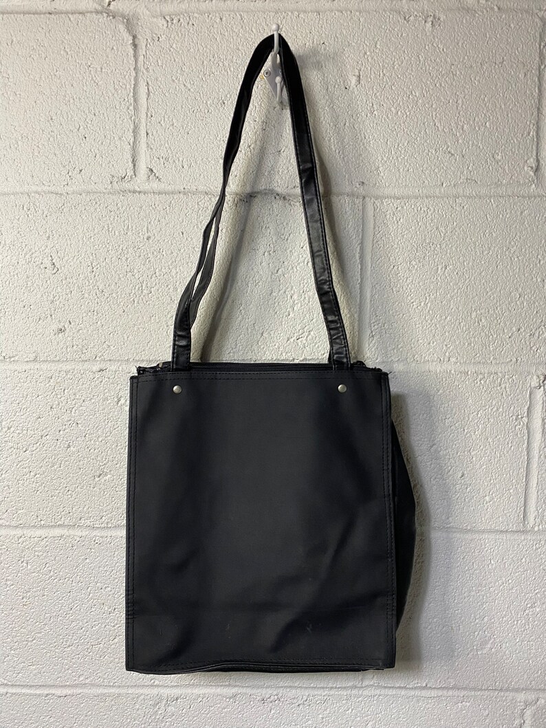 May include: A black tote bag with a black leather strap. The bag has a zipper closure and a flat base.