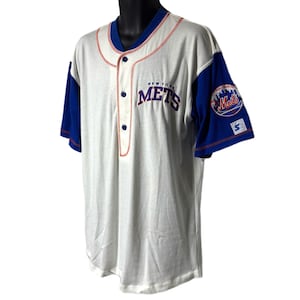 Può includere: Maglia da baseball bianca e blu dei New York Mets. La maglia presenta il nome della squadra in lettere blu sul petto, con cuciture rosse e maniche blu. Una toppa con il logo dei Mets è sulla manica sinistra.