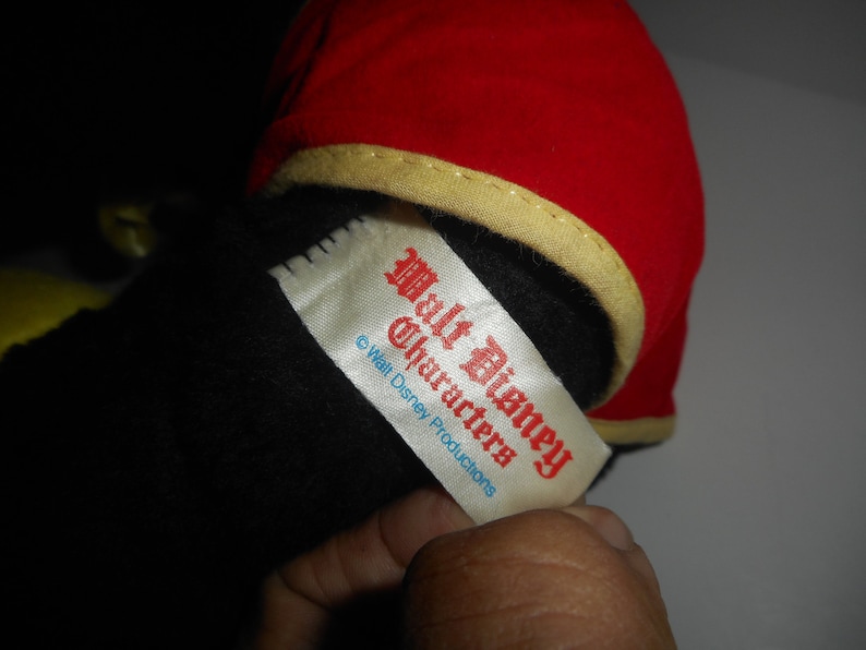 May include: A plush toy with a red hat trimmed with gold and a black body. A white tag with red text reads "Walt Disney Characters" and "&copy; Walt Disney Productions".