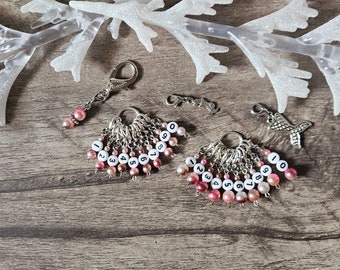 May include: Two sets of silver stitch markers with pink and white beads. Each set has ten markers numbered 0-9. The markers are attached to a silver lobster clasp. A silver mermaid charm is also included.