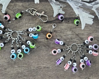 May include: A set of ten colorful keychains with numbers 0-9. Each keychain features a silver lobster clasp, black beads, and a bead with an evil eye design. The beads are in various colors, including pink, green, blue, and purple.