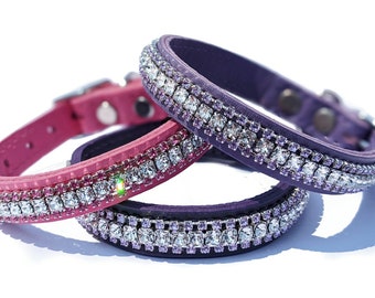 May include: Three dog collars in shades of pink and purple, each adorned with a row of sparkling rhinestones. The collars are made of leather and feature silver-toned buckles and hardware. The collars are designed for small dogs.