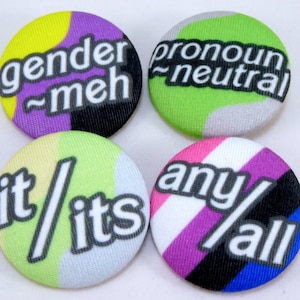 May include: Four round buttons with text and colorful backgrounds. The buttons say "gender meh", "pronoun neutral", "it/its", and "any/all". The buttons have a variety of colors including purple, green, pink, and black.