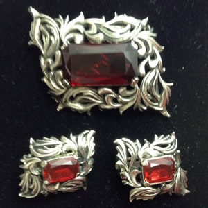 May include: A silver brooch and matching earrings with a red gemstone set in a filigree design.