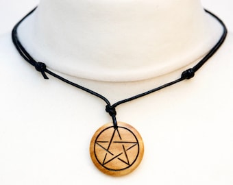May include: A wooden pendant necklace with a black leather cord. The pendant is round and features a carved pentagram.