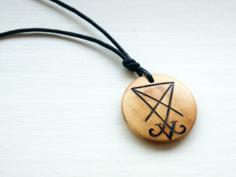 K&ouml;nnte beinhalten: Eine Holz-Halskette mit einem schwarzen Band. Der Anh&auml;nger ist rund und zeigt ein schwarz-wei&szlig;es Symbol eines Pentagramms mit einem Kreuz darin.