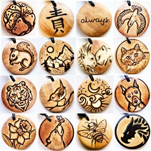 K&ouml;nnte beinhalten: Eine Sammlung von 16 runden Holzanh&auml;ngern mit verschiedenen Designs, darunter ein Eichh&ouml;rnchen, ein Tiger, ein Vogel, eine Katze, eine Biene, eine Blume, eine Berglandschaft, Mond und Sterne, ein L&ouml;we, ein Einhorn und das Wort "always".