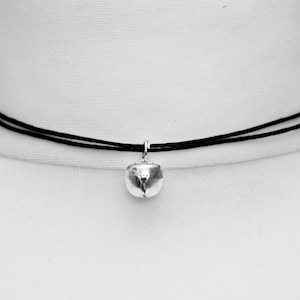 Tiny silver bell (1cm) on a 1mm black cotton cord choker that is adjustable and fits tightly around the models neck.