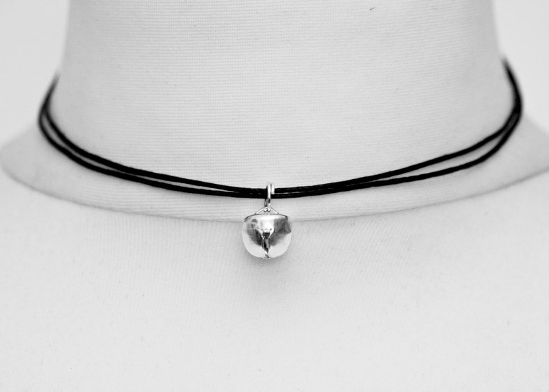 Tiny silver bell (1cm) on a 1mm black cotton cord choker that is adjustable and fits tightly around the models neck.