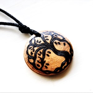 May include: A wooden pendant necklace with a black tree of life design. The pendant is round and has a black cord.