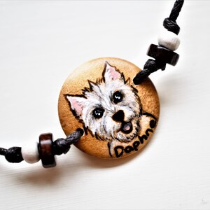 A bracelet with a wooden disc charm on an adjustable black cord with sliding knots.  The charm shows a wood burned design example of a pet dog, a highland terrier, persoanlised with the pets name underneath.