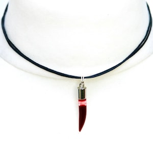 May include: A black cord necklace with a silver pendant shaped like a red fang.