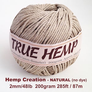 May include: A ball of natural hemp fiber with a label that reads "TRUE HEMP". The label also indicates the fiber's diameter, weight, and length. The text "Hemp Creation - NATURAL (no dye)" is also visible.