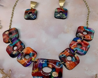 May include: A colorful necklace and earring set. The necklace features square, multi-colored pendants with gold accents, connected by a gold chain. The earrings have matching square pendants with gold-colored ear wires. The set has a unique, artistic design.