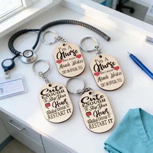 four wooden keychains with humorous sayings about nurses, placed on a white surface next to a stethoscope and a blue pen.