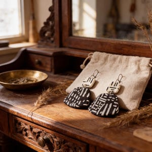 a pair of black and white patterned earrings resting on a wooden surface, with a small bowl and dried plant material nearby.