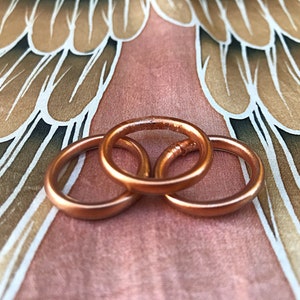 May include: Three copper rings stacked on top of each other. The rings are smooth and shiny, and they have a warm, metallic color.