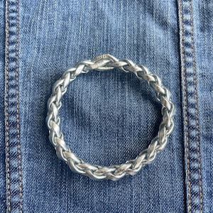 May include: A silver braided bracelet on a blue denim background.
