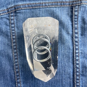 May include: A clear quartz crystal point with two silver rings inside. The crystal is sitting on a blue denim background.