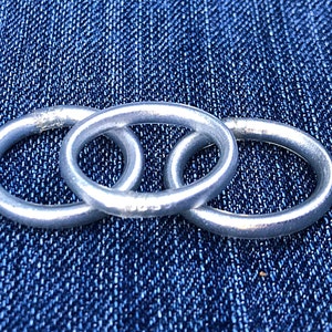 May include: Three silver rings interlocked together on a blue denim background.