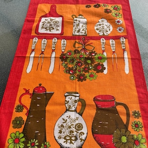 May include: A vintage kitchen towel with an orange background and a red border. The towel features illustrations of kitchen utensils, flowers, and pitchers in brown, white, and green. The design has a retro aesthetic.