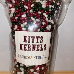 Puede incluir: Una bolsa de plástico transparente llena de granos de maíz para palomitas de maíz rojos, blancos y verdes. La bolsa tiene una etiqueta que dice "Kitts Kernels Rainbow Kernels".