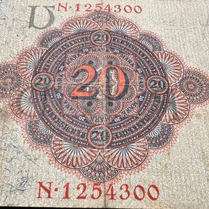 May include: An aged 20 Mark German banknote with an intricate, circular design in red, black, and white. The number "20" is prominently displayed in orange. The serial number "N 1254300" is visible.