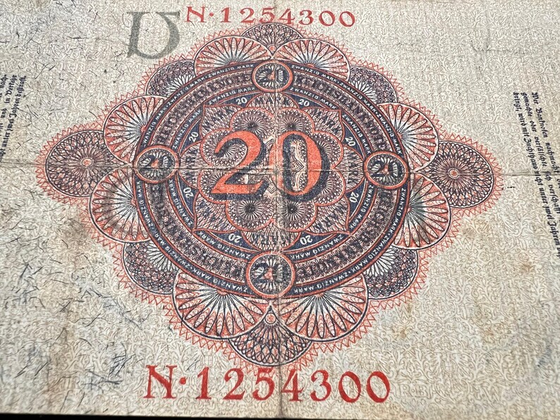 May include: An aged 20 Mark German banknote with an intricate, circular design in red, black, and white. The number "20" is prominently displayed in orange. The serial number "N 1254300" is visible.