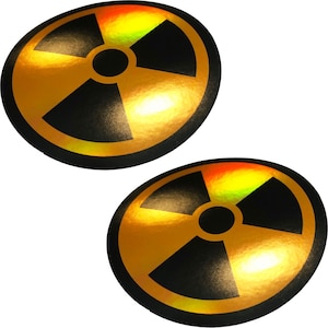 May include: Two oval-shaped stickers featuring the radiation symbol. The symbol is a black trefoil within a gold circle, with a black border. The stickers have a holographic, iridescent finish, reflecting yellow, orange, and green hues.