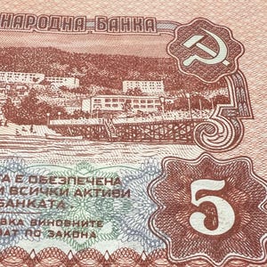 May include: Close-up of a vintage Bulgarian 5 lev banknote. The bill features a detailed illustration of a seaside town, the text "НАРОДНА БАНКА", and a hammer and sickle emblem. The number "5" is prominently displayed.