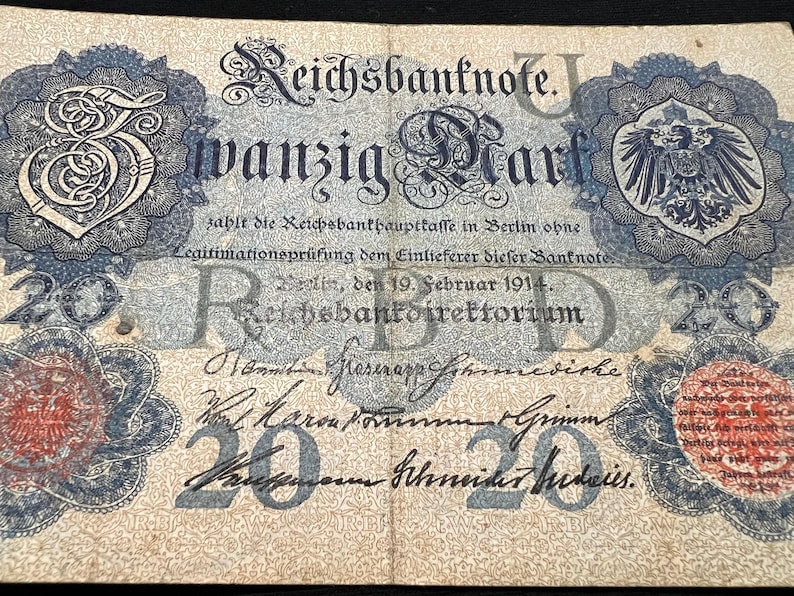 May include: A vintage German Reichsbanknote, featuring ornate blue and red decorative elements. The note displays the text "Reichsbanknote" and "zwanzig Mark" along with the date "19. Februar 1914". The number "20" is prominently displayed.