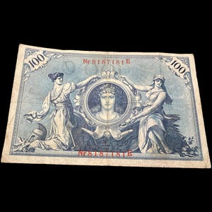 May include: A vintage 100 currency note with a light blue background. The note features two classical figures flanking a central portrait within an ornate frame. The text "100" appears in the corners, and the serial number "Nr 8187181E" is visible.