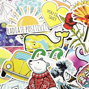 May include: A collection of colourful stickers featuring various designs, including a whale, a sunflower, a VW Beetle, a polar bear, a wave, a pineapple, and a star. The stickers have white borders and are arranged in a random pattern.