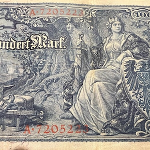 Könnte beinhalten: Ein antiker 100-Mark-Geldschein mit einer sitzenden Frau, die ein Schwert und einen Schild hält. Die detaillierte Gravur umfasst einen Baum, Schiffe und den Text "Ein Hundert Mark". Die Banknote hat rote Seriennummern und einen dekorativen Rand.