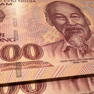Puede incluir: Primer plano de moneda vietnamita, con un retrato de Ho Chi Minh y la denominaci&oacute;n "50000". El billete tiene un patr&oacute;n detallado en tonos de rojo, rosa y amarillo.