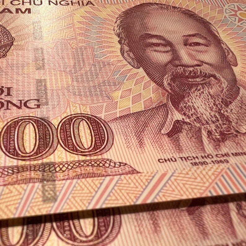 Puede incluir: Primer plano de moneda vietnamita, con un retrato de Ho Chi Minh y la denominaci&oacute;n "50000". El billete tiene un patr&oacute;n detallado en tonos de rojo, rosa y amarillo.