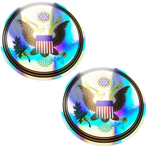 May include: Two iridescent round stickers with the Great Seal of the United States. The seal features an eagle with outstretched wings, holding an olive branch in its right talon and arrows in its left talon. The eagle is perched on a shield with thirteen stripes and a blue field with white stars. The seal is surrounded by a gold circle with the words "E Pluribus Unum" and "United States of America" inscribed on it.