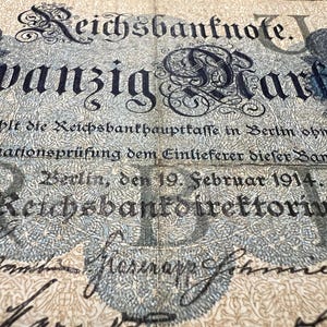 May include: An antique German Reichsbanknote, featuring ornate typography and intricate floral designs. The text includes "wanzig Mark" and the date "19. Februar 1914." The banknote is in shades of blue and cream.