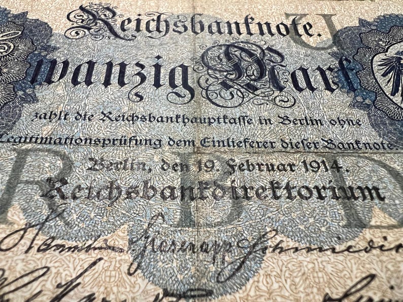 May include: An antique German Reichsbanknote, featuring ornate typography and intricate floral designs. The text includes "wanzig Mark" and the date "19. Februar 1914." The banknote is in shades of blue and cream.