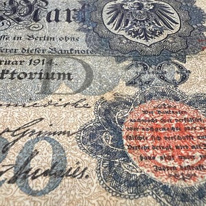 May include: Close-up of an antique German banknote, featuring intricate designs and text. The note displays the number "20" prominently, along with German text and a detailed emblem. The paper has a vintage, aged appearance.