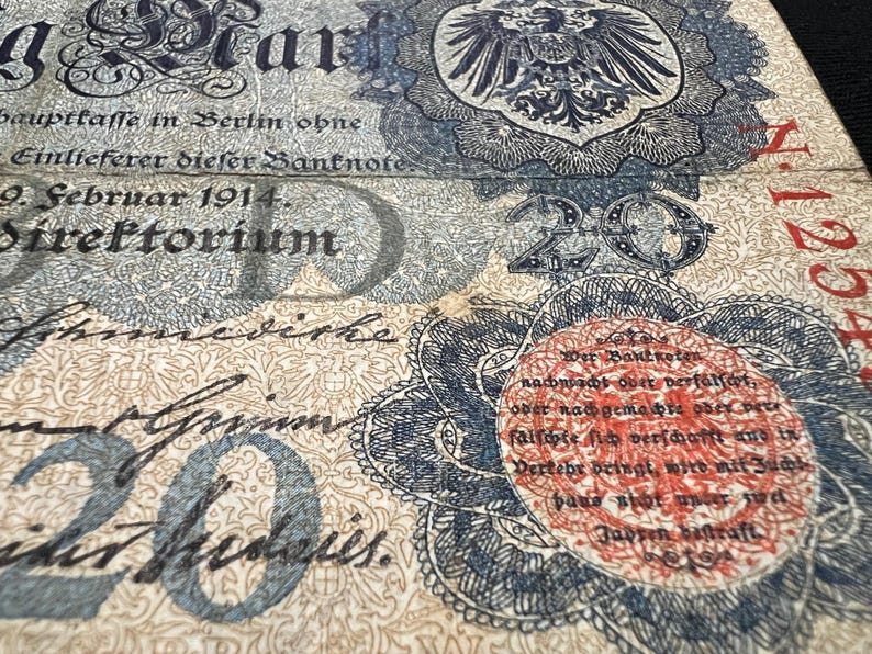 May include: Close-up of an antique German banknote, featuring intricate designs and text. The note displays the number "20" prominently, along with German text and a detailed emblem. The paper has a vintage, aged appearance.