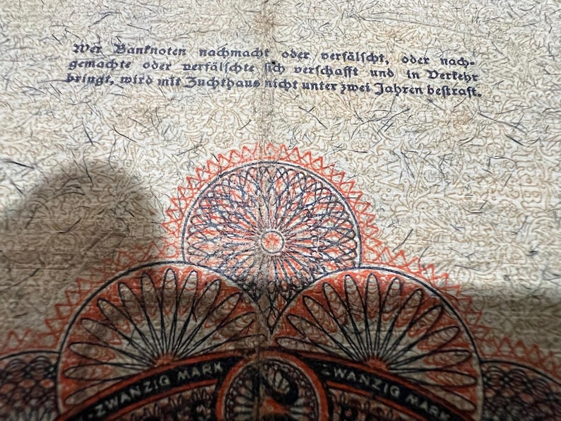 May include: Close-up of a vintage German 20 Mark banknote. The note features intricate circular designs in red, black, and orange. Text in German is visible at the top, with the words "ZWANZIG MARK" at the bottom.