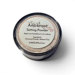 May include: A round, clear plastic container filled with beige setting powder. The label reads: Arrowroot Setting Powder, Apply over foundation to set makeup, Ingredients: Arrowroot Powder, Natural Clay, LittleStuff4u.com, with a leaf graphic.