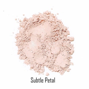 May include: A close-up of a pile of loose, light pink powder with a subtle shimmer. The powder is labeled "Subtle Petal".