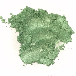 May include: A pile of loose, fine-grained powder with a vibrant, metallic light green color. The texture appears soft and shimmering, with individual particles reflecting light to create a bright, pearlescent finish across the irregular mound.