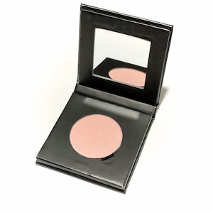 May include: A black compact with a mirror and a round, pink blush. The blush is in a pan with a black rim.