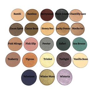 May include: A collection of twenty-two circular eyeshadow pans arranged in a grid. Each pan features a unique color including shades of brown, pink, green, gold, silver, purple, and black. The names Bambi, Bamboo, Berrywood, Black Smoke, Chantilly Lace, Cocoa Spice, Cocoa Bean, Honey Bee, Lucky Penny, Mocha Ice, Pink Mirage, Pink Slip, Pewter, Safari, Sea Breeze, Teaberry, Tigress, Trinket, Twilight, Vanilla Bean, Velveteen, Winter Moss, and Wisteria are printed on each pan.