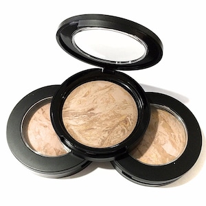 May include: Three round black compacts with a swirl pattern of light and dark brown shades of foundation. The compacts have a clear lid on top.